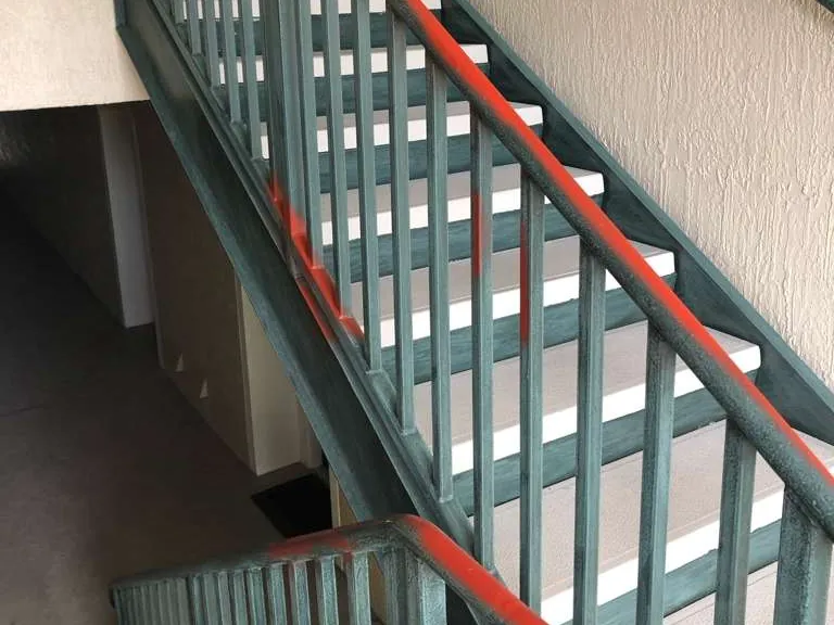 A building stairwell before, with worn green railings and red primer on the handrail