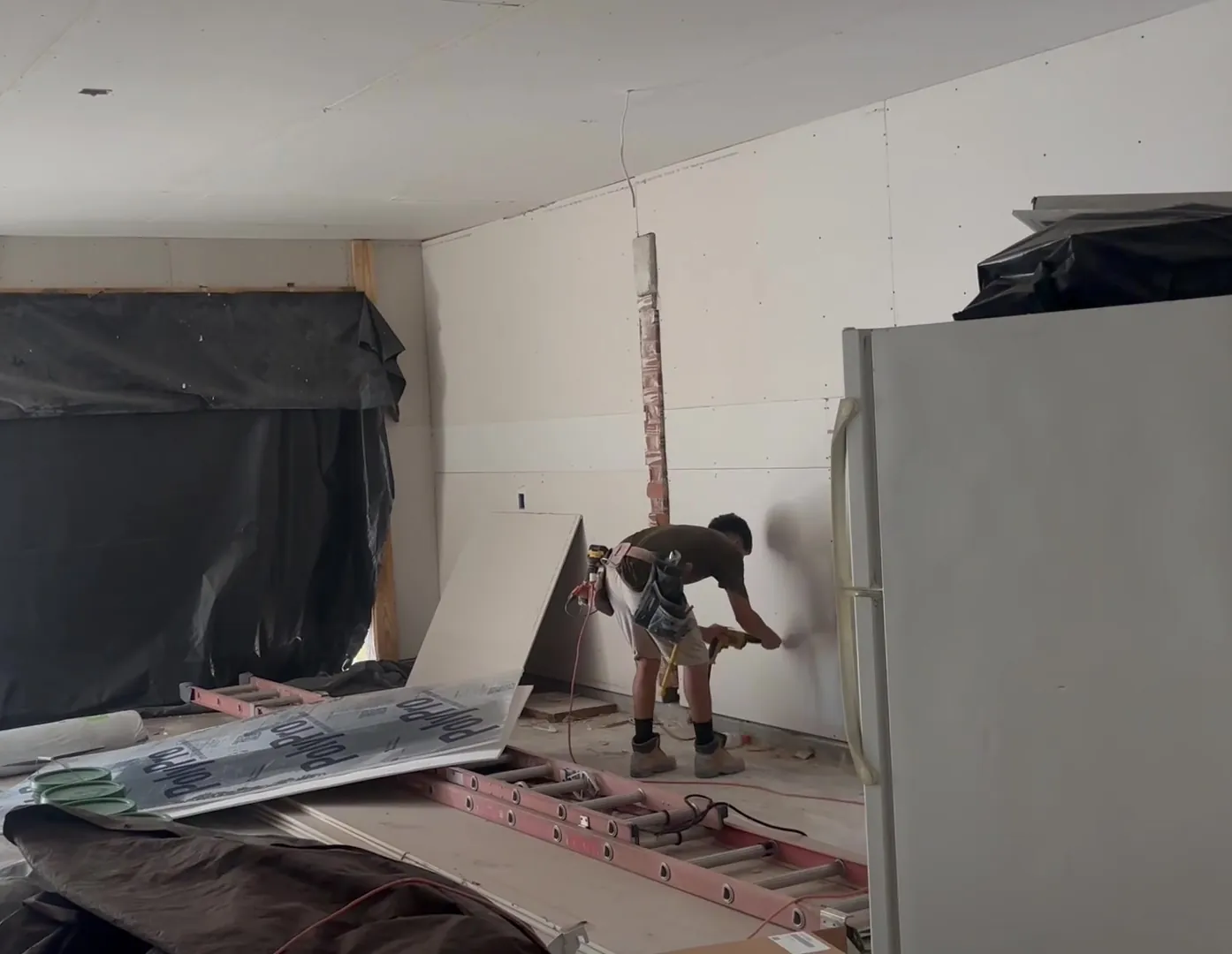 A Pristine Coastal crew member fastening new drywall while the room&rsquo;s contents stay covered