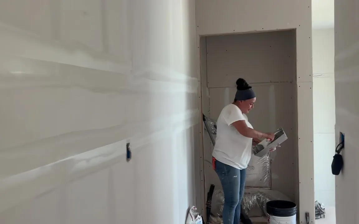 A crew member mudding new drywall from a hawk in a corner alcove