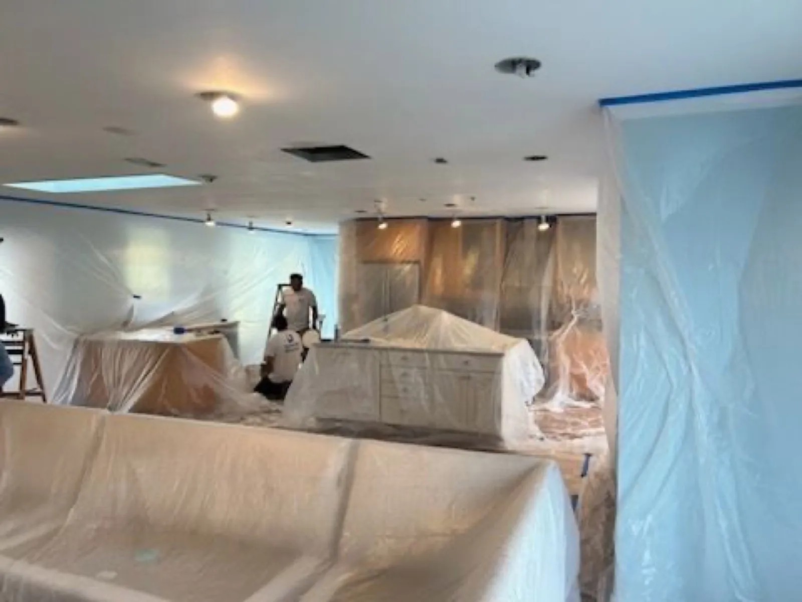 Interior under full plastic containment while a painter sprays